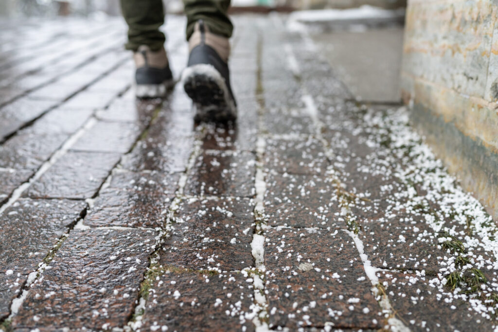 Closeup of technical salt grains on icy sidewalk surface in winter, used for melting ice and snow.